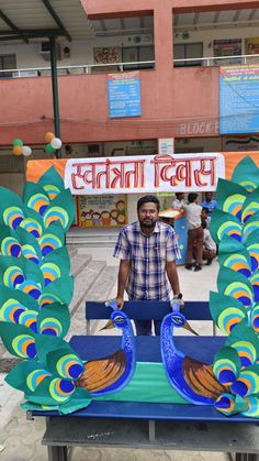 a man standing in front of a fake peacock display on a table with lots of blue and green feathers