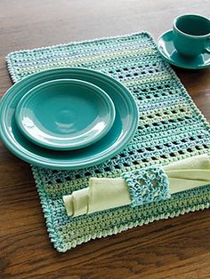 a crocheted place setting with two cups and saucers on the table top