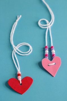 two heart shaped necklaces are hanging from strings on a blue surface with white string