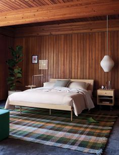 a bedroom with wood paneling and a bed in the corner, next to a green chair