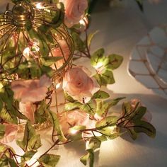 some pink roses and green leaves on a table with lights in the background at night