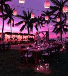 an outdoor dining area with palm trees and lanterns hanging from the ceiling, surrounded by grass