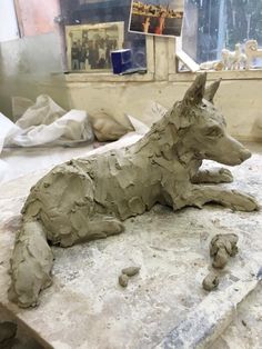 a clay sculpture of a dog laying on top of a stone slab in a studio