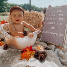 a baby sitting in a tub with some pine cones on the ground next to it