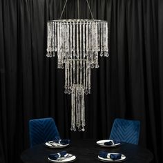 a chandelier hanging from the ceiling over a dining room table with blue chairs