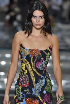 a model walks down the runway in a black and multicolored print mini dress