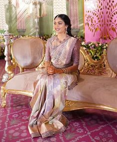 a woman sitting on top of a couch in front of a pink and gold wall