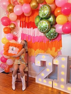 a woman sitting on a chair in front of a wall with balloons and garlands