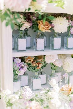 there are many small vases with flowers on the shelves next to each other in front of them