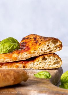 two pieces of pizza sitting on top of a wooden cutting board next to some basil leaves