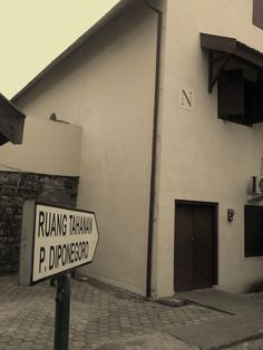 a street sign in front of a white building with black shutters and an awning