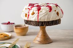 a cake with white frosting and cranberry toppings on a wooden stand