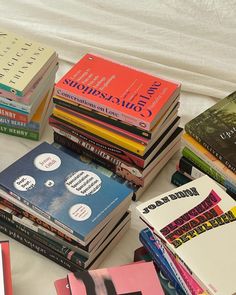 a pile of books sitting on top of a white bed next to each other in front of a curtain