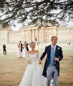 a bride and groom walking in front of a large building with people standing around it