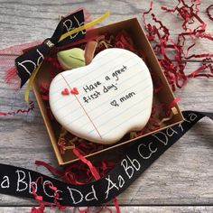 an apple shaped cookie in a box with writing on the side and ribbon around it