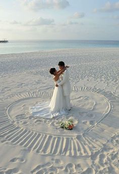 a bride and groom standing in the middle of a circle on the beach with their arms around each other