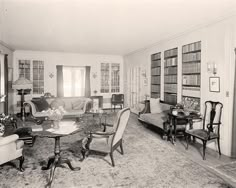 an old black and white photo of a living room filled with chairs, couches and bookshelves