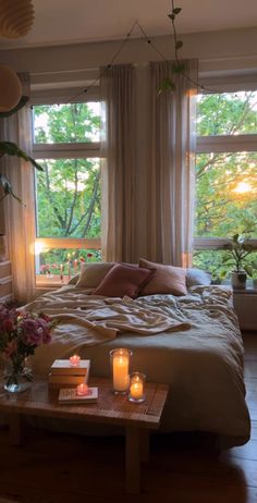 a bed sitting in a bedroom next to two windows with candles on top of it