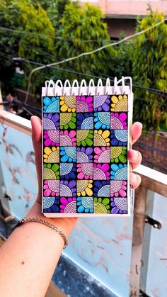 a hand holding up a notebook with colorful designs on it