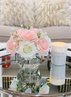 a glass table with flowers and candles on it in front of a white fur pillow