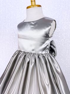 A classic and simple but beautiful full satin dress that's perfect for any formal occasion: weddings, graduations, birthdays, or holidays! Handcrafted with the upmost of care and attention to detail, we make sure that each dress is perfectly one of a kind for your little girl. Comfortable satin material covers the dress from shoulder to hem. The sleeveless top has a zipper on the back for closure. Comes with a detachable matching bow with tails. The skirt has a layer of lining underneath with at Pageant Photoshoot, Silver Satin Dress, Photoshoot Graduation, Wedding Bridesmaid Flowers, Pageant Costumes, Silver Gown, Party Photoshoot, Sleeveless Gown, Wedding Flower Girl