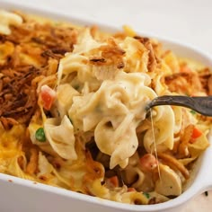 a casserole dish with noodles, meat and vegetables being spooned into it