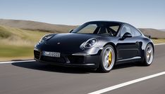 a black porsche sports car driving down the road with hills in the distance behind it