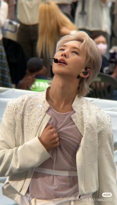 a woman with her eyes closed standing in front of a crowd wearing earbuds