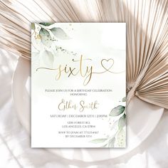 a white and gold birthday party card with greenery on the front, surrounded by palm fronds