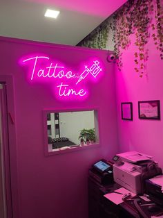 a pink room with a neon sign that says tattoo time on the wall next to a printer