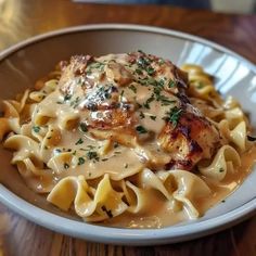 a white bowl filled with pasta and chicken covered in gravy on top of a wooden table