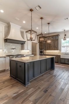 a large kitchen with an island in the center and two pendant lights hanging from the ceiling