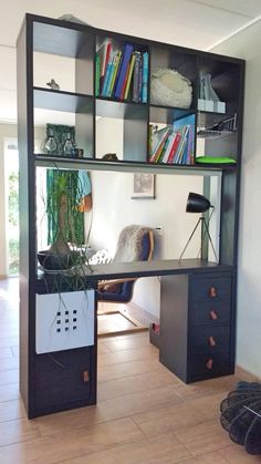 a desk with bookshelves and plants on it in the middle of a room