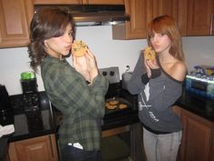 two women standing in a kitchen eating cookies