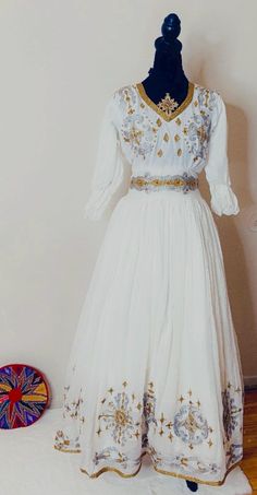 Ethiopian and Eritrean traditional dress (habesha kemis)beautiful traditional dress  i predominantly white with detailed golden and silver embroidery on the bodice, sleeves, and along the bottom of the flowing skirt. The design includes intricate patterns, elegant dress Habesha Kemis For Graduation, Simple Habesha Kemis, Ethiopian Culture, Silver Embroidery, Uniform Fashion