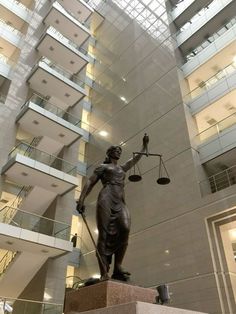 a statue of lady justice in front of a building with glass walls and balconies