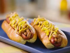 two hotdogs with mustard and onions on a blue plate, ready to be eaten