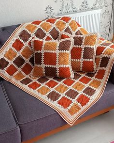 a crocheted blanket and two pillows on a couch in front of a radiator