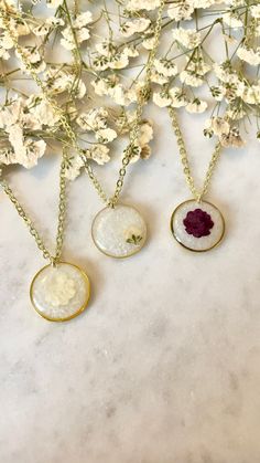 three necklaces with flowers in them sitting on a table next to some white flowers