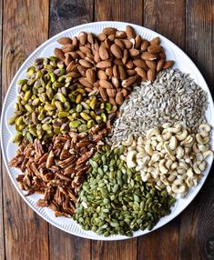 a white plate topped with different types of nuts and seeds on top of a wooden table