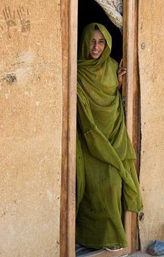 a woman in a green shawl is looking out the doorway to her right and smiling