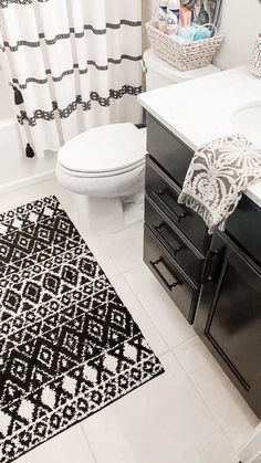 a white toilet sitting next to a black and white rug on top of a bathroom floor