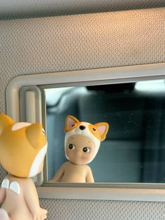 a toy cat sitting in front of a mirror next to a stuffed animal on the side of a car