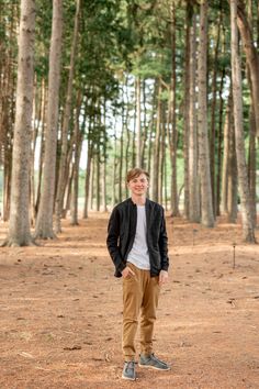 a man standing in the middle of a forest with trees around him and smiling at the camera