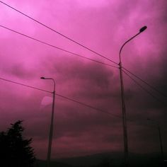 the sky is very dark and pink with some power lines in front of it,