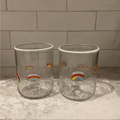 two glasses with rainbows painted on them sitting on a counter top next to a brick wall