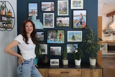 a woman standing in front of a blue wall with pictures and plants on the walls