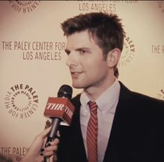 a man wearing a suit and tie holding a microphone in front of a wall with the paley center for los angeles