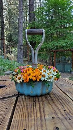 a blue planter filled with flowers sitting on top of a wooden table in the woods