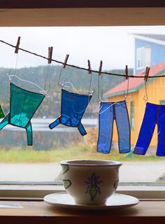 a cup and saucer sitting on a window sill next to clothes hanging from a line